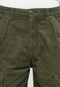 Pantalones cargo de pana en verde oscuro con canalé vertical, que cuentan con bolsillos frontales y un cierre de botón en la cintura.