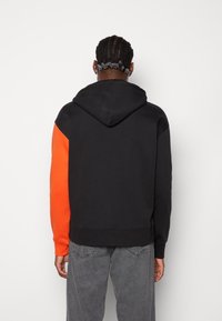 Sudadera de mezcla de algodón, con un cuerpo negro y mangas de un vibrante color naranja. Cuenta con capucha con cordón y puños acanalados.