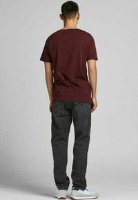 Vinröd kortärmad t-shirt tillsammans med mörka denimjeans och vita sneakers. T-shirten har en rund halsringning och jeansen har bakfickor.