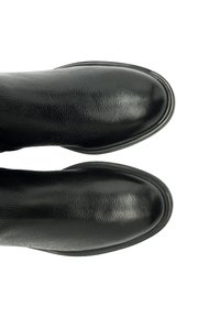 Botas de cuero negras con punta redonda, textura suave, brillo sutil y suela delgada blanca en contraste a lo largo del borde.