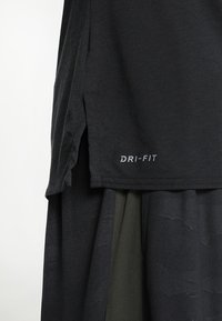 Svart DRI-FIT-topp med korta ärmar, som har en sidesslits för förbättrad rörelse. Mjuk textur med en minimalistisk design.