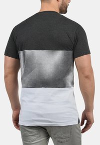 Camiseta de manga corta con parte superior gris oscuro, medio a rayas en blanco y negro, y parte inferior blanca sólida. Hecha de suave tela de algodón.