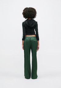 Μαύρο κοντό φούτερ με κουκούλα και λευκές ρίγες στα πλάγια, σε συνδυασμό με ψηλόμεσο, πράσινο παντελόνι με φαρδιά μπατζάκια και πίσω τσέπη.