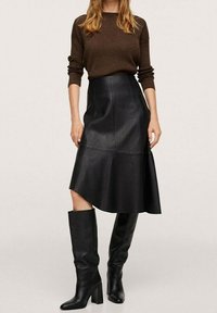 Jupe en cuir noir en ligne A avec des détails de couture, associée à un pull texturé marron et des bottes noires à talons hauts. Surface lisse, design ajusté.