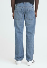 Ljusblå, löst sittande denimjeans med hög midja, synlig sömnad, två bakfickor och mjuk textur. Bärs tillsammans med vita sneakers.