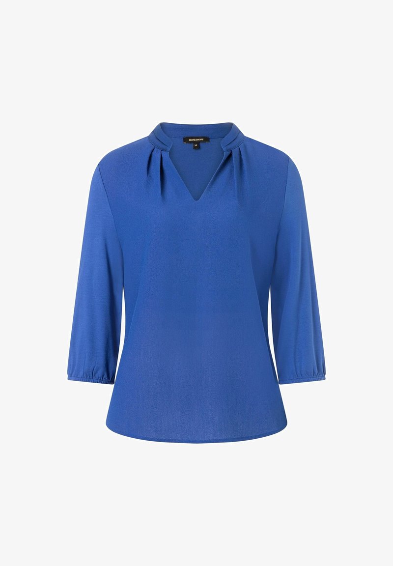 Blouse bleue à manches trois-quarts, col en V avec plis subtils et petit col montant.