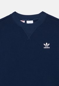 Μπλέ σκούρο υφασμάτινο sweatshirt της Adidas με στρογγυλή λαιμόκοψη και μικρό λευκό λογότυπο trefoil της Adidas στο αριστερό στήθος.