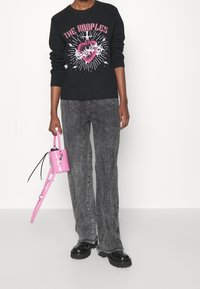 Czarna bluza z grafiką, szare dżinsy o wyblakłej fakturze, czarne masywne botki oraz mała różowa torebka na długim pasku.