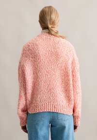 Grober Strickpullover in einer rosa- und cremfarbenen Farbmixtur, mit lockerer Passform, überschnittenen Schultern und geripptem Saum, kombiniert mit blauen Jeans.