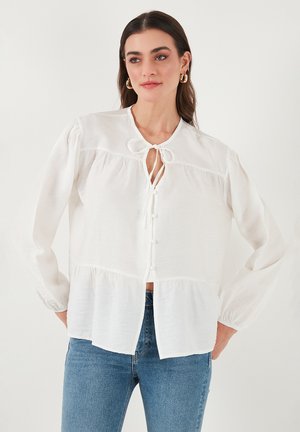 White blouse made of lightweight fabric, featuring a tie neck, button front, and gathered hem. Long sleeves with gathered cuffs.