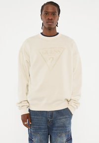 Beige sweatshirt met een ronde halslijn, voorzien van een subtiel driehoekig logo aan de voorkant. Gemaakt van zachte stof, met een relaxed fit en lange mouwen.