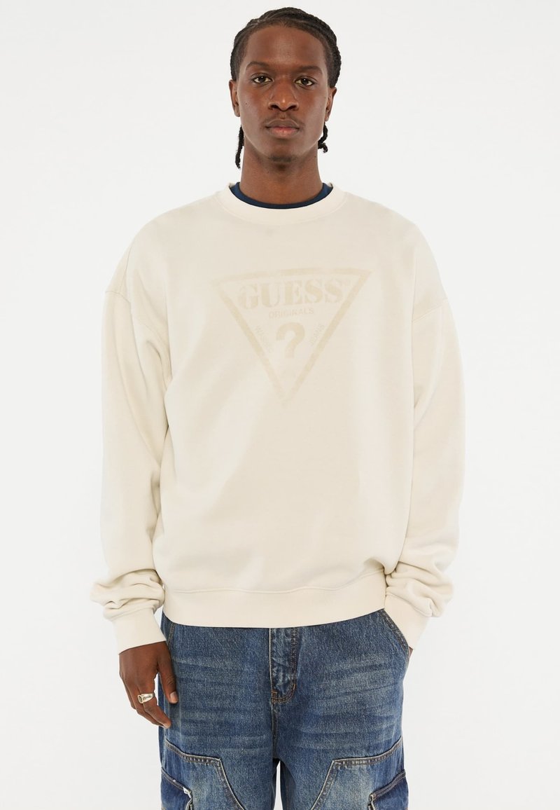 Felpa beige con scollo a girocollo, caratterizzata da un sottile logo triangolare sulla parte anteriore. Realizzata in tessuto morbido, con vestibilità rilassata e maniche lunghe.