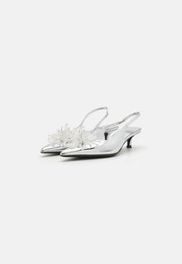 Srebrne slingback pete s ostrim prstom, z dekorativnimi prozornimi cvetličnimi poudarki in nizko peto. Gladka metalna tekstura.