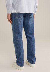 Losse donkerblauwe spijkerbroeken met een rechte pijp, voorzien van achterzakken en een lichte vervaging, in combinatie met witte sneakers.