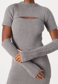 Robe grise en maille avec manches courtes, présentant une découpe rectangulaire. Le tissu est doux, texturé et côtelé, avec de longs chauffe-bras assortis.