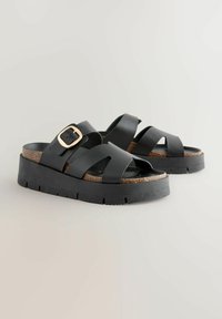 Sorte platform sandaler med kork sål, med brede krydsede stropper og en guldfarvet spændeaccent. Tekstureret gummisål for godt greb.