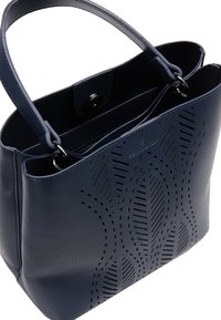 Tmavě modrá kožená taška ve stylu tote s perforovaným vlnkovým vzorem, dvěma uchy, magnetickým zapínáním a zipovou vnitřní kapsou.