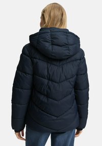 Marineblaue Steppjacke mit Chevron-Steppung, abnehmbarer Kapuze und elastischen Bündchen. Leichtes, gepolstertes Material bietet Wärme und Komfort.