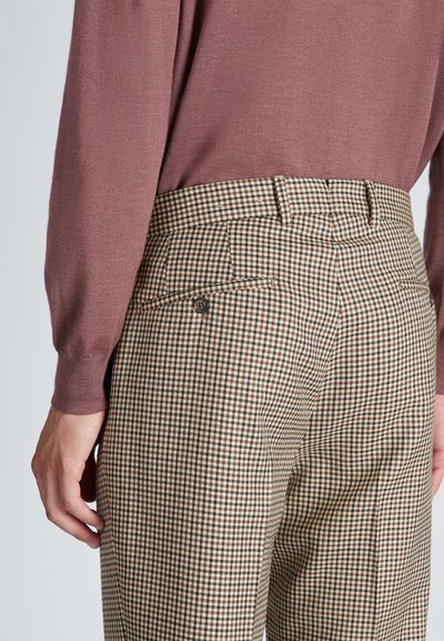 Bruine en crèmekleurige geblokte broek met een getailleerde pasvorm, voorzien van een achterzak en een knoopdetail, gedragen met een mauve gebreide trui.