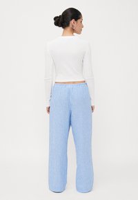 Blusa branca de mangas longas combinada com calças largas listradas em azul claro, apresentando uma cintura elástica e um ajuste confortável.