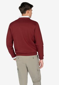 Bordowy sweatshirt z okrągłym dekoltem, ściągaczami przy rękawach i w pasie. Noszony na jasno-niebieskiej koszuli z kołnierzykiem w paski. Jasne khaki spodnie cargo.