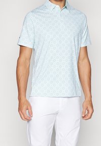 Pánské polo tričko s krátkým rukávem v světle modré barvě, s geometrickými vzory v zelené a bílé, a klasickým límečkem.