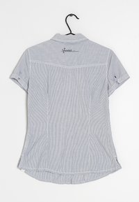 Kratší košile světle modré barvy s bílými vertikálními pruhy, límečkovým designem a vyšívaným logem na zádech. Dolní okraj je zaoblený s postranními rozparky.