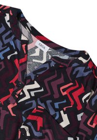 Bunt gestreifte Hemd mit einem Zickzackmuster in Rot, Blau und Weiß auf einem dunklen Hintergrund. Der Stoff ist weich, hat einen V-Ausschnitt und Knopfdetaillierung.