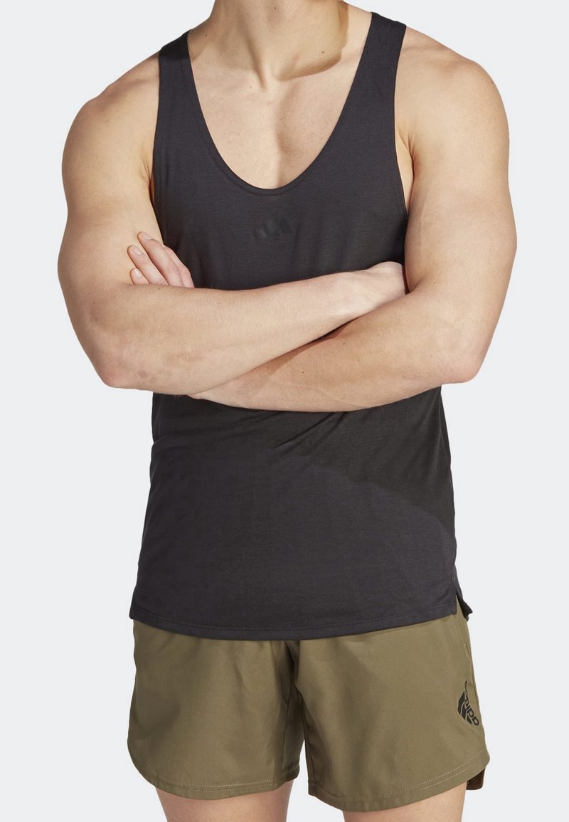 Débardeur de sport noir sans manches avec une texture lisse, arborant un petit logo sur la poitrine, accompagné d'un short vert olive.