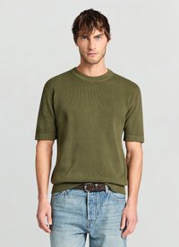 Pull à manches courtes en maille vert olive avec un col rond et des poignets côtelés, associé à un jean en denim bleu clair et une ceinture tissée.