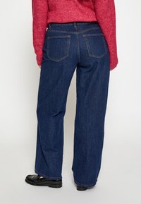 Jeans širokih nogavica od tamnog plavog denima s glatkom teksturom, s dva stražnja džepa i kontrastnim šavovima duž šavova.