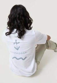 Camiseta de algodón blanca con un diseño de ancla, flecha y líneas onduladas en gris claro en la parte posterior. Corte casual, mangas cortas.