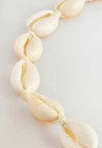 Naturlig muslingehalskæde lavet af glatte, blanke hvide cowrie-skjold, jævnt placeret og trædet med en tynd, beige snor.