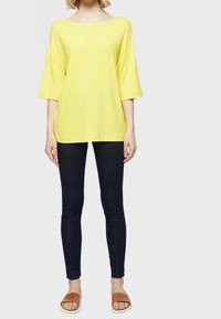 Žluté oversized tričko s širokým výstřihem a krátkými rukávy, spárované s tmavě modrými skinny džíny a béžovými nazouvacími sandály.