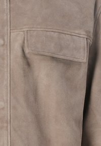 Beige suede shirt featuring a chest pocket, soft texture, and visible stitching details, highlighting its tailored design and fabric quality.