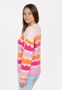 Kolorowy sweter z dzianiny z paskowanym wzorem w zygzaki w kolorze różowym, pomarańczowym i kremowym. Prążkowane mankiety i dół, okrągły dekolt. Miękka tekstura.