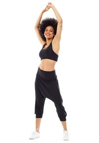 Sujeción deportiva negra y pantalones cortos negros de corte ancho, confeccionados en una tela suave, con una cintura alta y puños fruncidos en los tobillos.