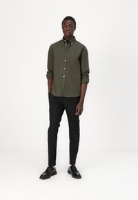 Cămașă cu nasturi de culoare verde închis, cu guler, purtată împreună cu pantaloni negri slim-fit și pantofi negri lucioși. Design stilat și contemporan.