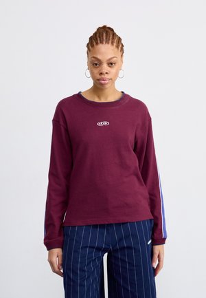 Maroon long-sleeve shirt with a round neckline and logo on the chest, paired with navy pinstriped trousers. Cotton material, relaxed fit.