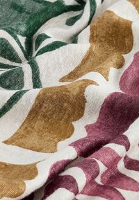 Tissu doux avec un motif de grandes formes de feuilles abstraites vertes, marron et violettes sur fond blanc.