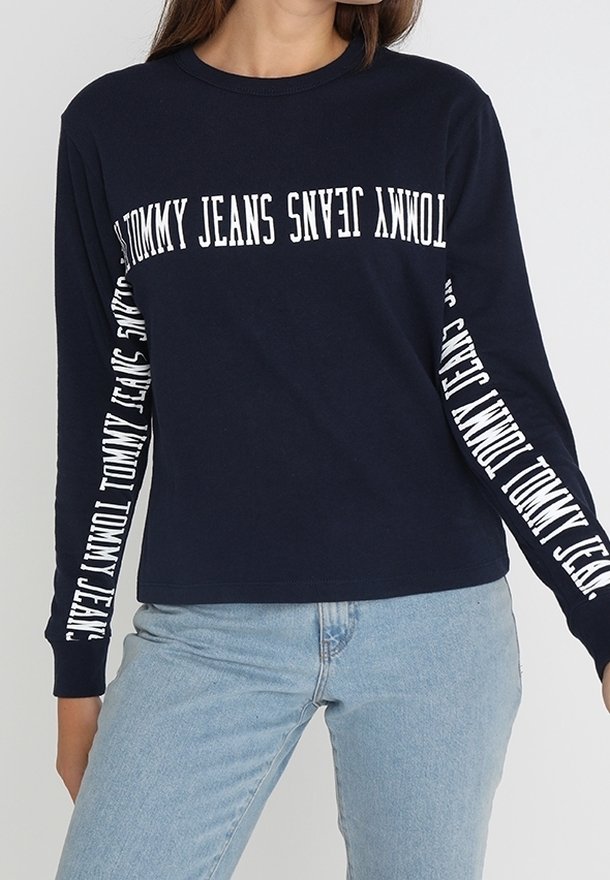 Navy long-sleeve t-shirt in cotton featuring white "TOMMY JEANS" text printed across the front and along both sleeves. Classic fit design.
