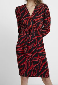 Schwarzes Kleid mit rotem abstraktem Muster, Wickeldesign, langen Ärmeln, tailliertem Gürtel und tiefem Ausschnitt. Glatte Stofftextur.