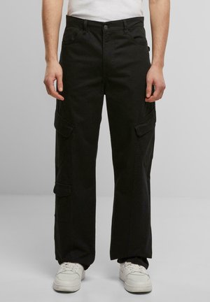 Black cargo pants made of cotton, featuring large side pockets, a straight-leg design, and a button closure. Worn with white sneakers.