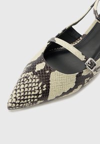 Zapatos de punta con un diseño de estampado de serpiente en negro y crema. Cuenta con una correa ajustable con una hebilla plateada y un interior negro suave.