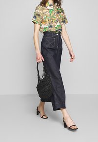 Košile s krátkým rukávem s vícerozměrným zvířecím potiskem, spárovaná s kalhotami s vysokým pasem z tmavého denimu a černou tkanou taškou.