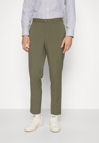 Olive roheline püksid slim-fit lõikega ja sirgete jalgadega, millel on ees nööp-kinnitus. Kombineeritud valgete tossudega ja triibulise särgiga.