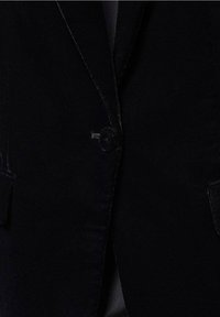 Blazer en velours noir avec une fermeture à un bouton, des revers crantés et deux poches avant, présentant une texture lisse et douce.