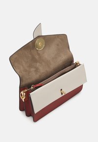 Strukturovaná kabelka v červené a krémové kůži s semišovým interiérem, vybavená zlatým uzávěrem a kapsou na zip.