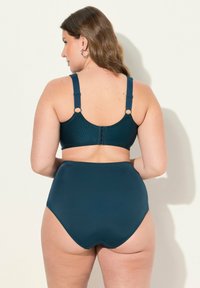 Top in bikini color teal con pois testurizzati e spalline regolabili, abbinato a slip a vita alta in tinta unita teal. Finitura in tessuto liscia.