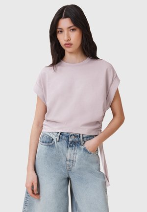 Jasnofioletowy krótkoterminowy t-shirt z podwiniętymi krótkimi rękawami, z detalem sznurków po bokach, zestawiony z wysokim stanem wyblakłymi niebieskimi dżinsami.